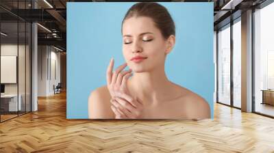 Young woman applying hand cream on color background Wall mural