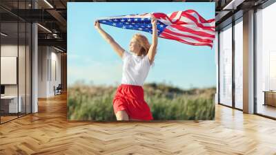 Young woman holding American flag on blue sky background Wall mural