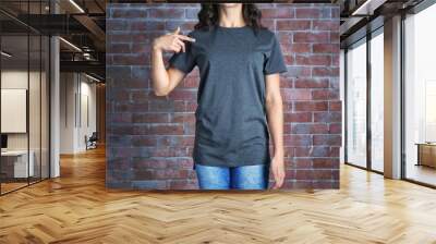 Young woman in blank grey t-shirt standing against brick wall, close up Wall mural