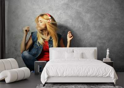 Young woman sitting on the floor and listening to music on a grey wall background Wall mural