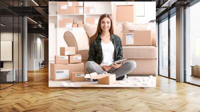 Young woman with tablet computer preparing parcel for shipment to client at home Wall mural