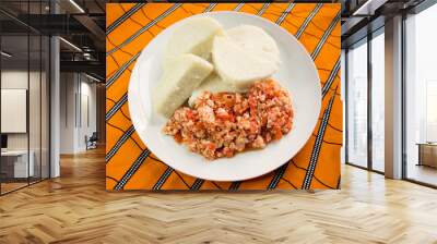 A white plate of boiled yam and fried scrambled eggs prepared with sliced onions, tomatoes and red pepper. Ready to eat and served on a colorful orange African pattern table cloth Wall mural