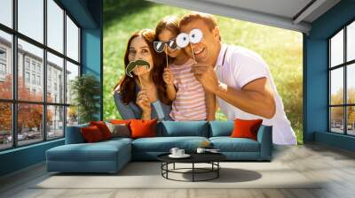 happy girl, woman and man using funny paper masks on the sticks in the park and looking at the camera Wall mural