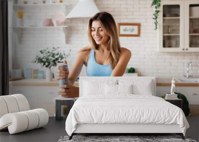 Slim young woman smiling while preparing a green smoothie Wall mural