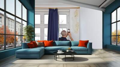 Man taking a photo of a big patch of mold or mildew growing behind the drapes of a white external wall in an old house. Wall mural