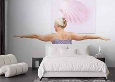 Senior woman with gray hair doing yoga exercises in front of a wall with a picture, home fitness concept, asana warrior II Wall mural