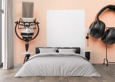 Flat lay shot of professional headphones and a radio microphone with a blank sheet of paper in the center, on a light peach background. Podcast and radio concept. Wall mural