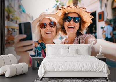 Two friends in their 50s smile happily as they take a selfie with their smartphone during a walk in the city. Wall mural