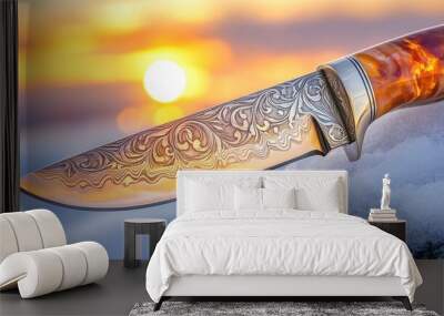 A  close-up of a sharp hunting knife resting on a snow-covered rock, with a bright orange sunset in the background. Wall mural