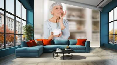 charming elderly woman applying cosmetic cream on her face for facial skin care in bathroom Wall mural