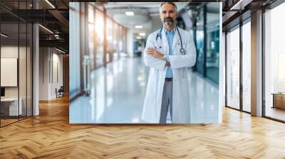 Portrait of friendly middle aged european male doctor in workwear with stethoscope on neck posing with folded arms in clinic interior, looking and smiling at camera, free space Wall mural