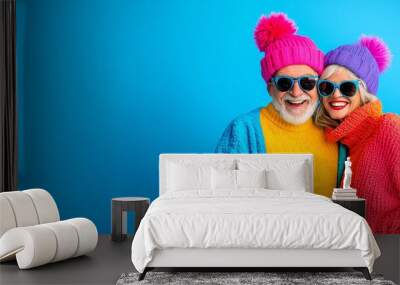 Stylish senior couple wearing sunglasses and bright clothing against a blue background. Wall mural