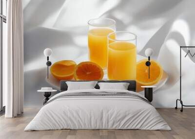 Two glasses of orange juice and orange slices on a white plate with white fabric background. Wall mural