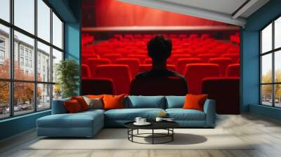 Solitary figure sits in theater's red seat, gazing ahead, cinematic ambiance Wall mural