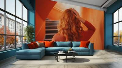 Back view of unrecognizable young redhead female standing in building with orange walls near staircase adjusting hair  Wall mural