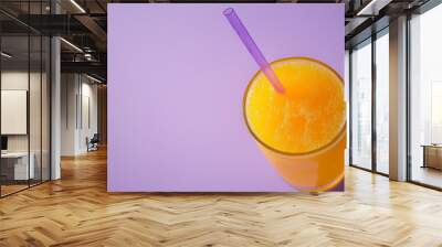 orange juice in glass with straw on a purple background. Wall mural