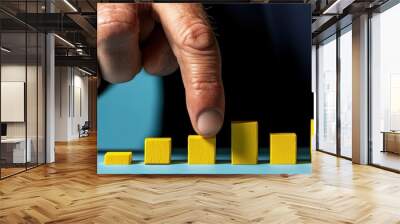 Close-up of a businessman's hand holding a bar on a yellow 3D bar chart, representing growth and progress in a business or financial context, on a blue background. Wall mural