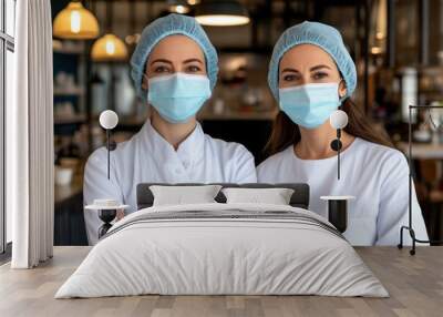 Two healthcare professionals in masks and caps pose confidently in a modern cafe setting, emphasizing teamwork and safety. Wall mural