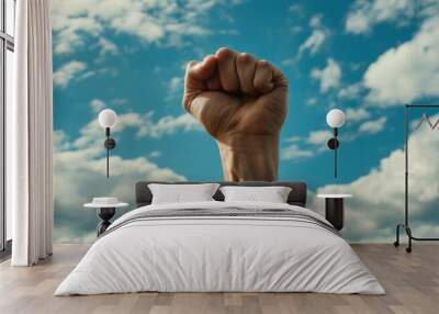 A fist raised in defiance against a backdrop of vibrant clouds, symbolizing unity and strength. Wall mural