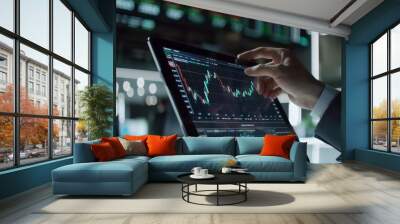 A hand manipulates a digital trading app on a tablet, focusing intensely on the fluctuating financial graphs, nearby markets visible in a sleek design. Wall mural