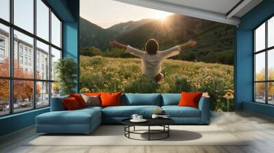 A person embraces the vastness of a wildflower-strewn mountain meadow, arms wide, as the sun sets behind distant peaks, epitomizing peace and connection with nature. Wall mural