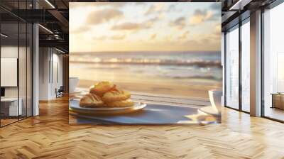 A tranquil seaside breakfast scene with coffee and pastries on a table, with the sun rising over the horizon, casting a golden light on the beach. Wall mural