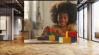 A young girl, smiling brightly, performs a playful activity with colorful blocks in a warmly lit room, radiating happiness. Wall mural