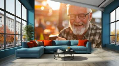 An elderly man gleefully looks at his phone in a sunny outdoor café, radiating joy and connection. Wall mural