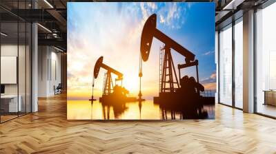 Oil well pumpjacks silhouetted against the setting sun in an oil field Wall mural