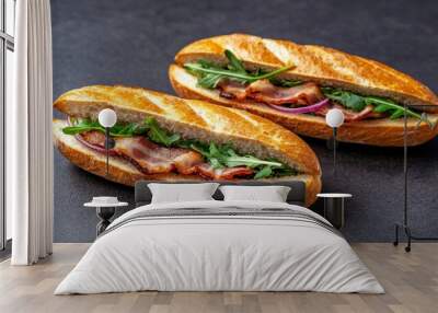 Two baguette sandwiches with bacon, arugula, and red onion on a dark background Wall mural