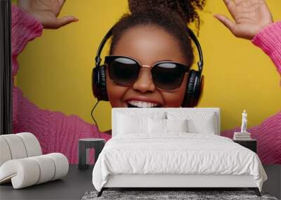 Young woman with headphones listening to music wearing pink sweater on yellow background. Wall mural