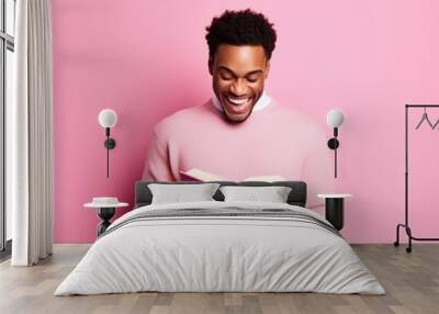 Cute African American young man toothy smile hold read opened book isolated on pink color background Wall mural