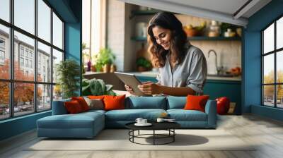 Happy millennial young woman cooking dinner in home kitchen, using tablet computer at table with vegetables, dish, reading online recipe, watching organic food blog Wall mural