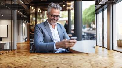 Happy smiling relaxed mid aged business man, mature professional businessman entrepreneur sitting in outdoor cafe holding smartphone using mobile phone digital technology apps Wall mural