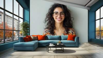 Young Arabian woman with glasses, smiling brightly with a friendly demeanor, standing against a soft light grey background. Wall mural