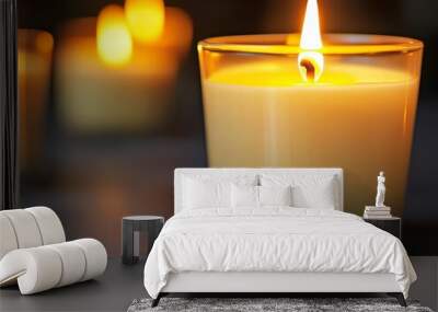 A single lit candle in a glass jar, with two other candles out of focus in the background. Wall mural