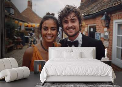 A cheerful couple dressed in formal attire smiling happily at an outdoor event with rustic brick buildings and festive decorations in the background Wall mural