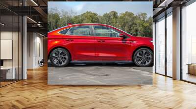 A striking red sedan car captured in a serene outdoor setting by a riverside amidst lush greenery and blue skies, showcasing its sleek design and modern aesthetics Wall mural