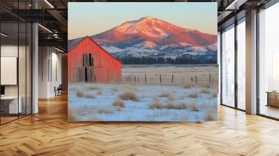 An isolated red barn stands in a snow-covered field with a majestic mountain in the background, illuminated by the warm colors of the setting sun Wall mural