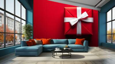 Charming red gift box decorated with white ribbon on a red surface, creating a cheerful atmosphere for Christmas or Valentine's Day celebrations or surprises. Wall mural