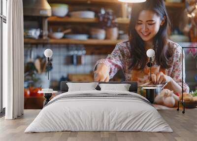 A woman is cooking in her kitchen. She is wearing a floral shirt and an apron, and she is smiling while stirring a pot.. asian woman Wall mural