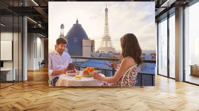 Travel, breakfast and couple in Paris with the Eiffel Tower on a terrace for romance or anniversary. City, vacation or tourism tech app with a man and woman eating food while looking at a view Wall mural