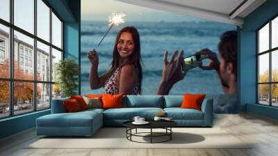 Beautiful woman holding sparkler posing for photo on romantic beach celebrating new years eve at sunset Wall mural