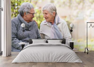 Two elderly women sitting on bench in park smiling happy life long friends enjoying retirement Wall mural