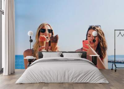 Two friends taking photos of ice cream eating on beach using smart phone technology on adventure travel Wall mural