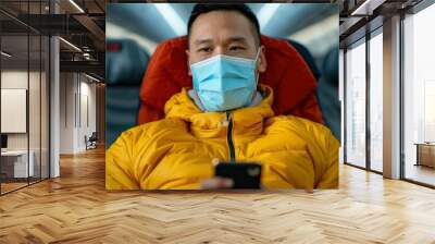 An Asian Young Man Traveler In The New Normal, Holding A Smartphone In The Airplane Lounge, Wearing A Blue Face Mask Wall mural