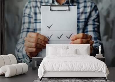 Man Holding Checklist on Clipboard with Three Check Marks in Casual Plaid Shirt Against Abstract Background Wall mural