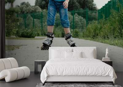 Little boy in protective equipment and rollers stands on walkway in park, low angle view Wall mural