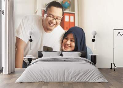 Asian muslim couple smiling happy when looking at smart phone, good news on internet Wall mural