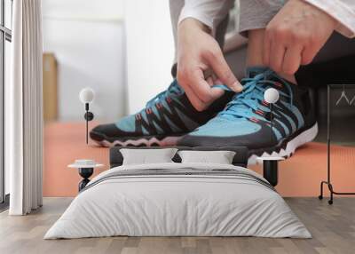 Young Asian muslim woman tying her shoelaces in her bedroom, preparing for workout, indoor home exercise Wall mural